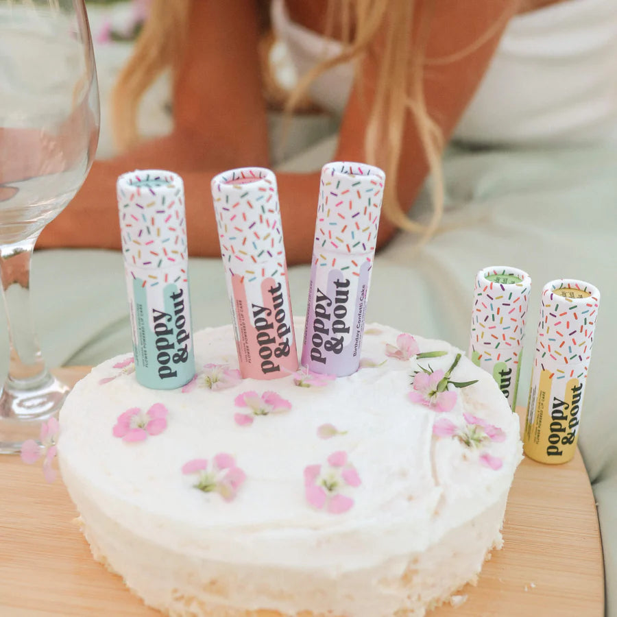 Cake with lip balm tubes on top, featuring 'Poppy & Pout' branding.