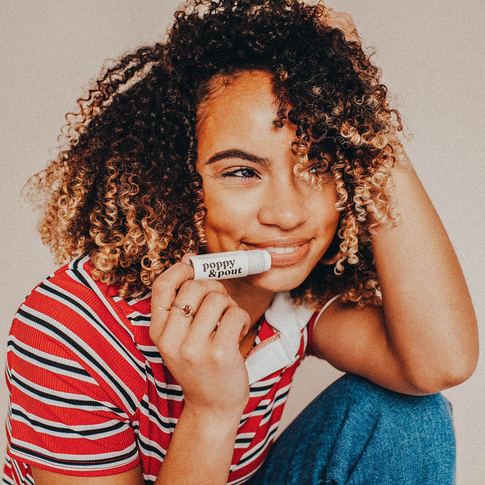 Woman holding a product labeled 'Poppy & Pout' against a neutral background