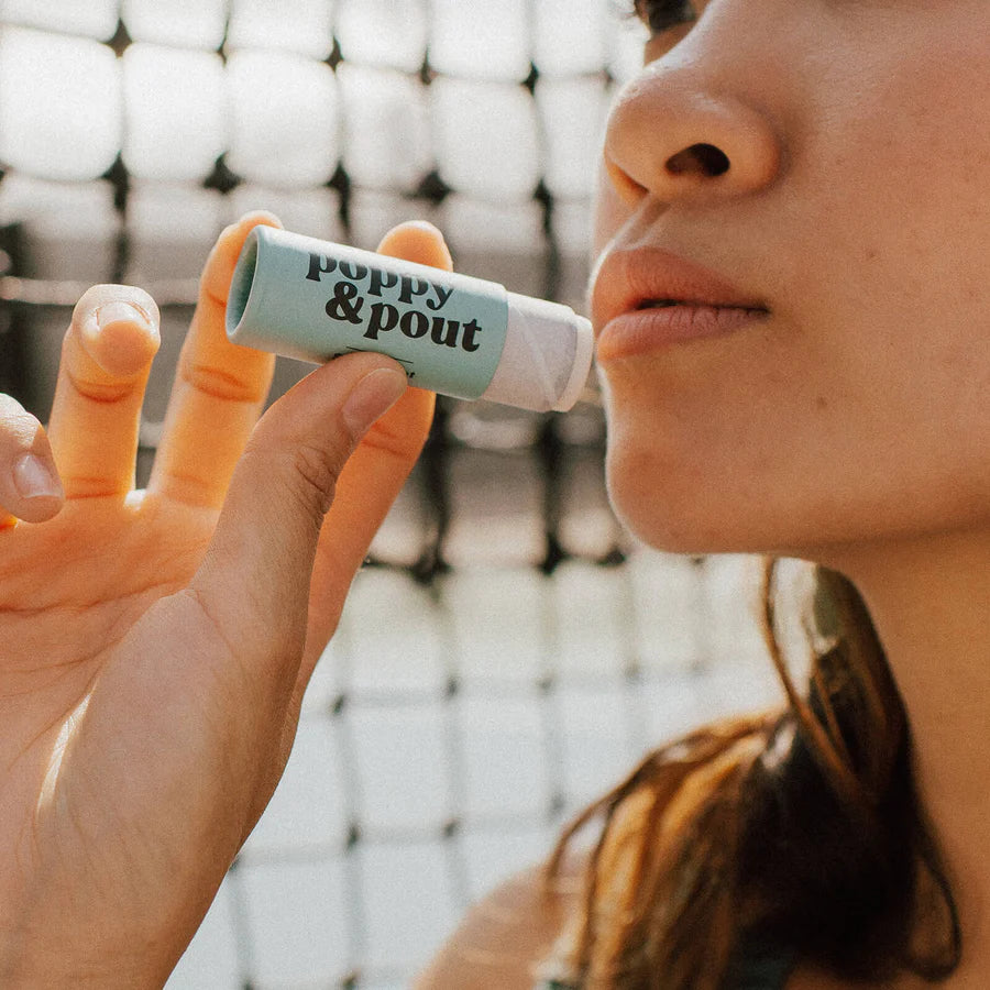 Person holding a lip balm labeled 'poppy & pout' with a blurred background