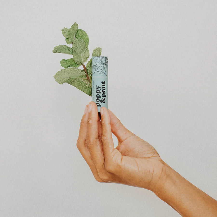 Hand holding a small cylindrical product with green leaves on a light background