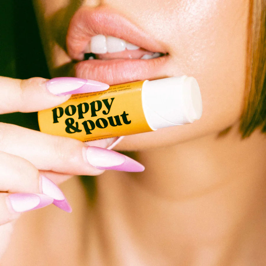 Lip balm with 'poppy & pout' branding held by a person with pink nail polish.