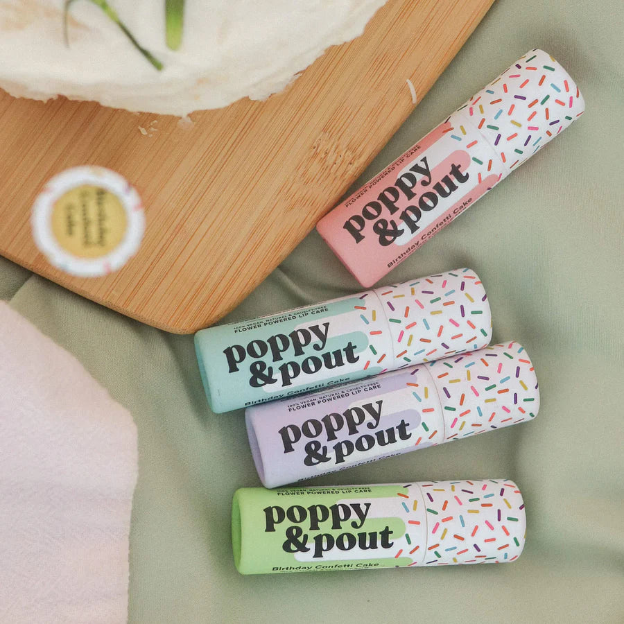 Four lip balm tubes with 'Poppy & Pout' branding on a light green surface.