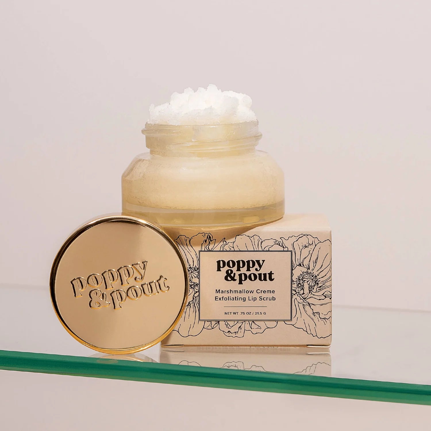 Poppy & Pout lip scrub jar and packaging on a clear surface with a light background