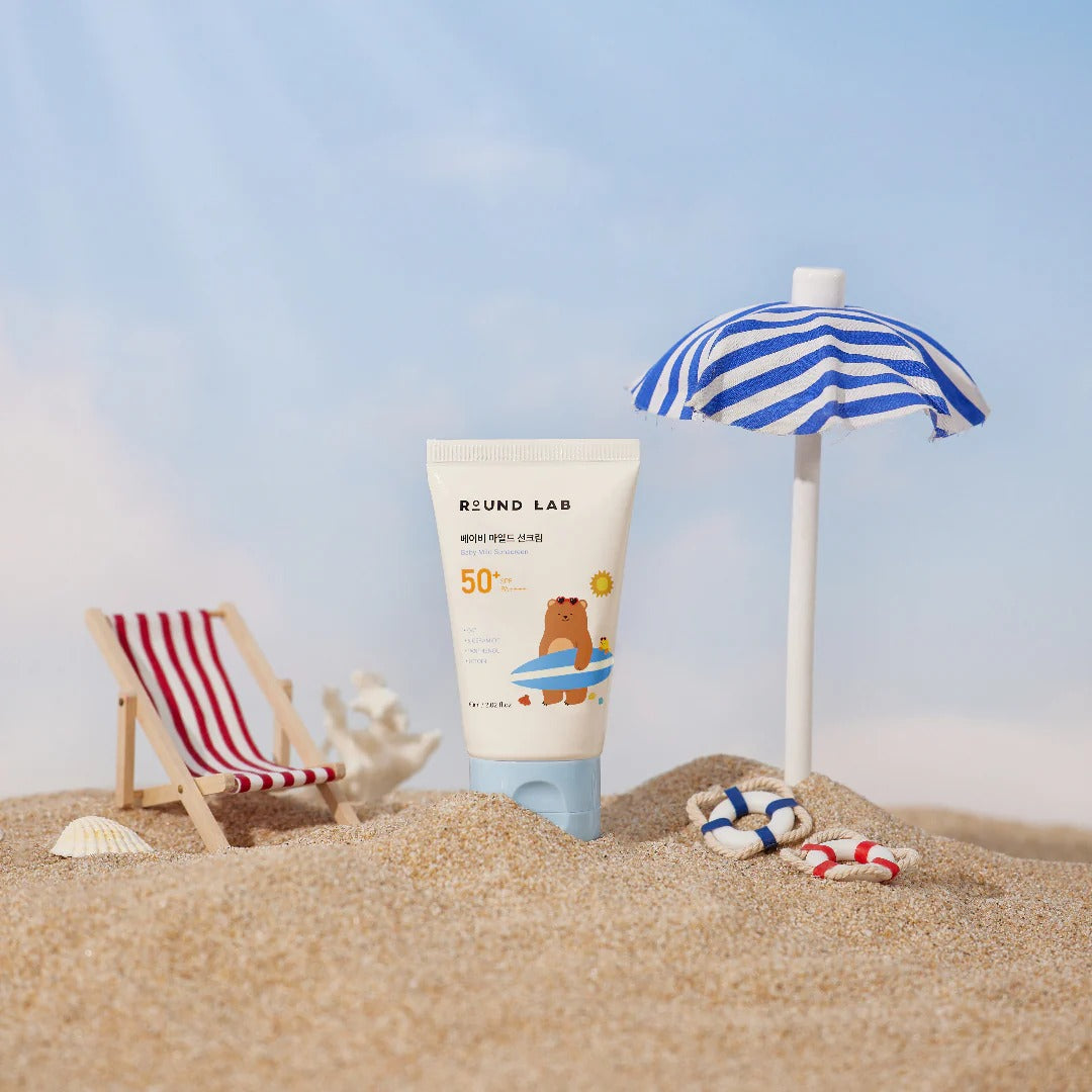 Sunscreen tube with bear design on a sandy beach with a striped umbrella and chair.