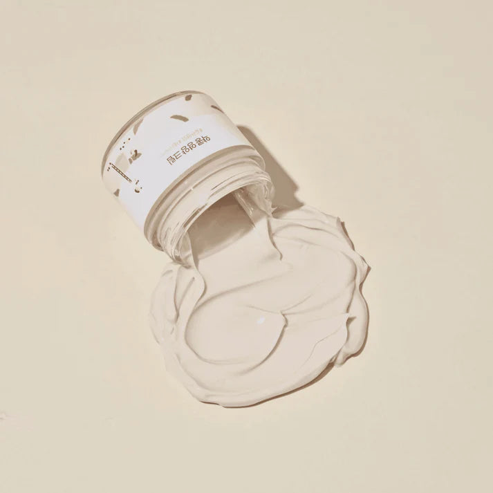 Open jar of cream with a swatch on a beige background