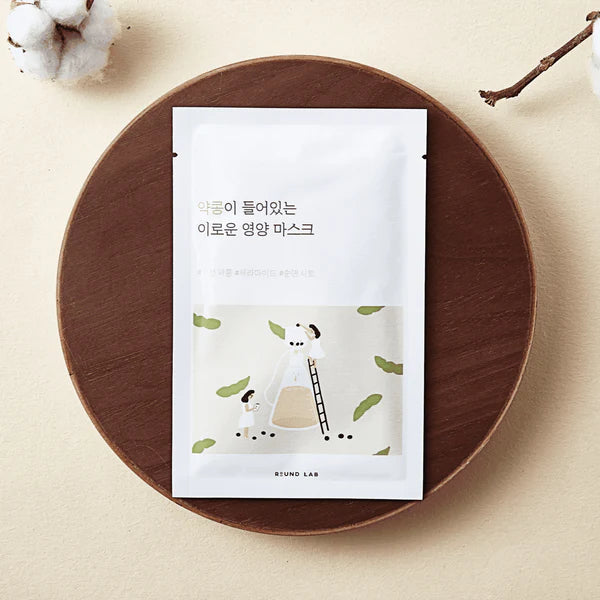 White sheet mask packaging on a wooden plate with cotton and branch in the background
