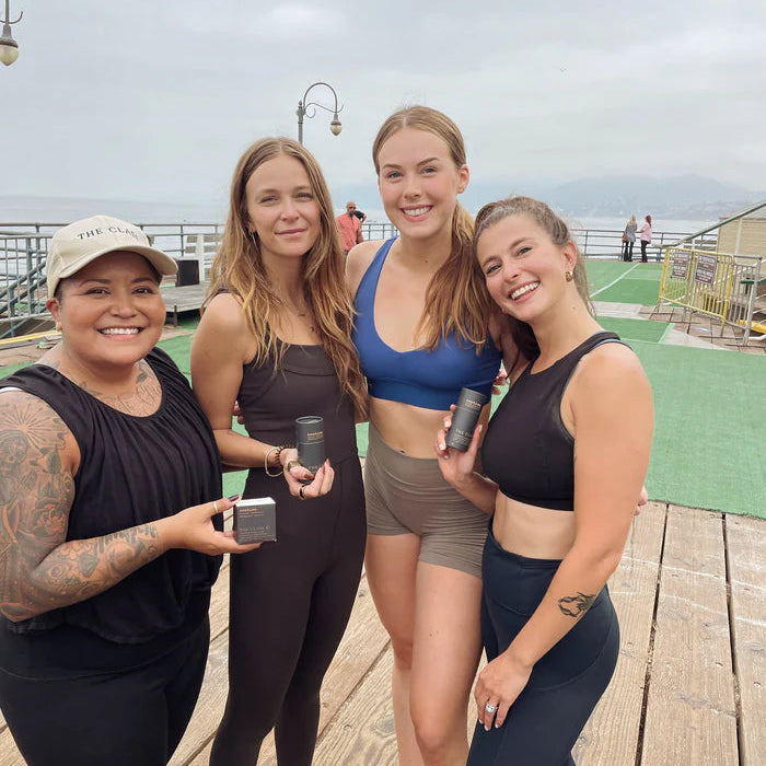 Four women posing together on a wooden pier with a cloudy sky.