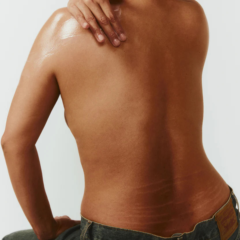 Person applying oil to their back with a neutral background