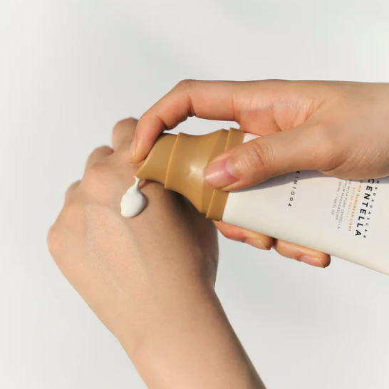 Hand applying cream from a bottle with a visible brand name on a light background
