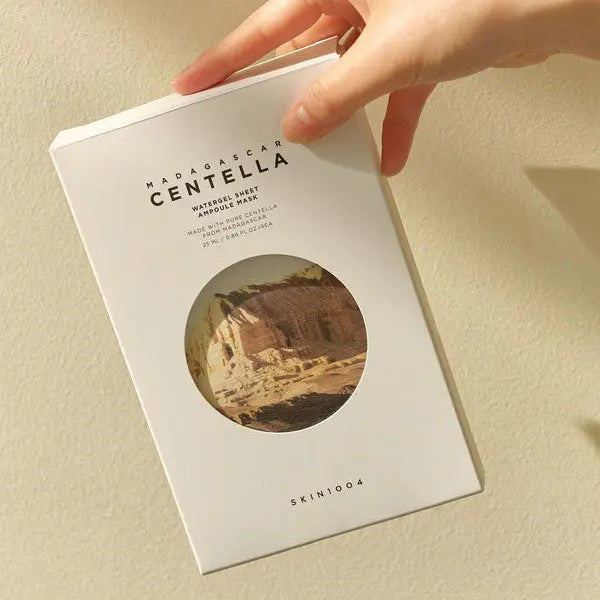 Hand holding a skincare product packaging with 'Madagascar Centella' text on a beige background