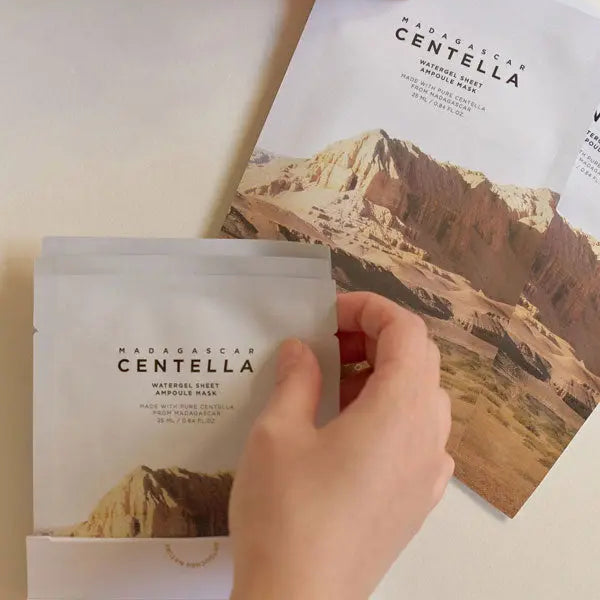 Hand holding a Madagascar Centella product package with a mountain-themed background