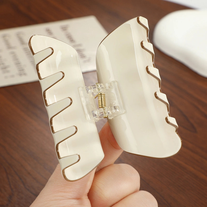 White hair clip with wavy design held by a hand on a wooden surface.