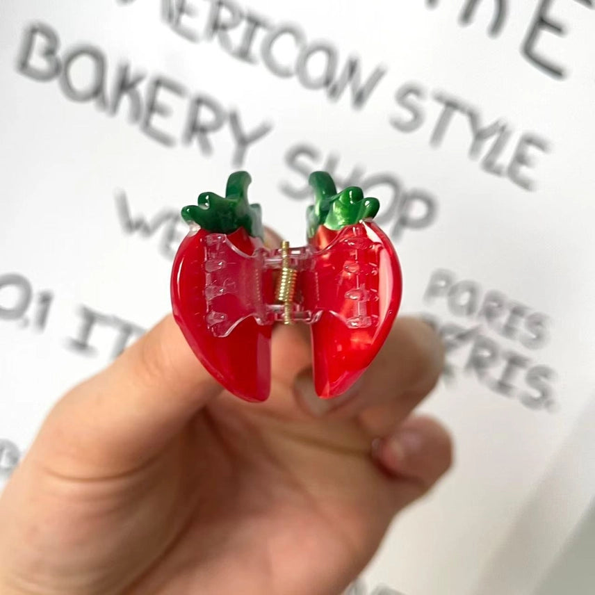 Red strawberry-shaped hair clip held by a hand with a blurred background