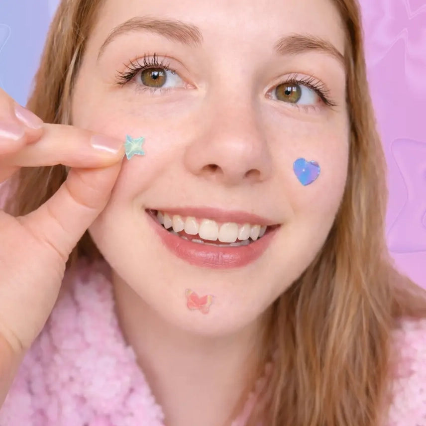 Person with decorative stickers on their face against a pink background