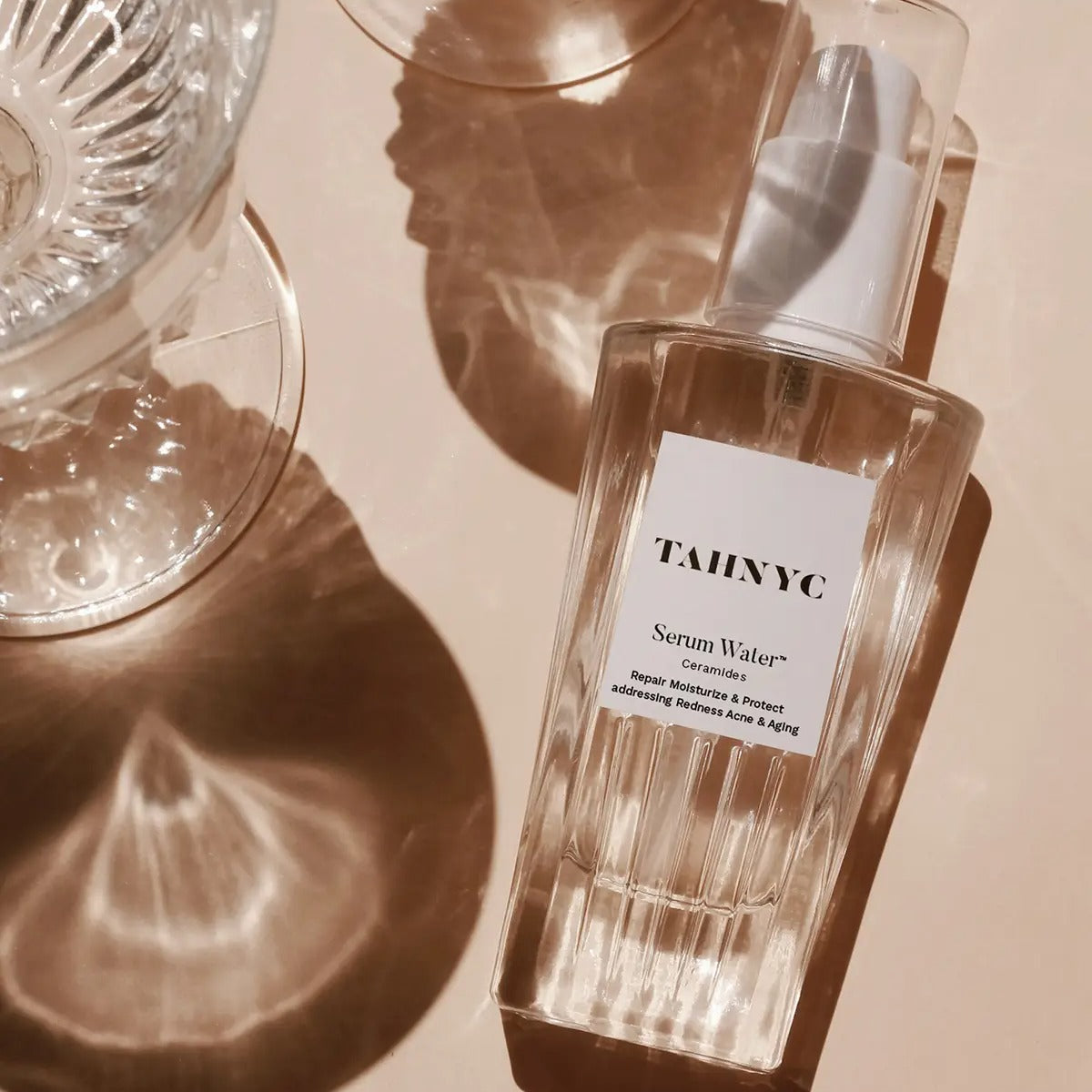 Tahync serum water bottle on a beige surface with soft shadows