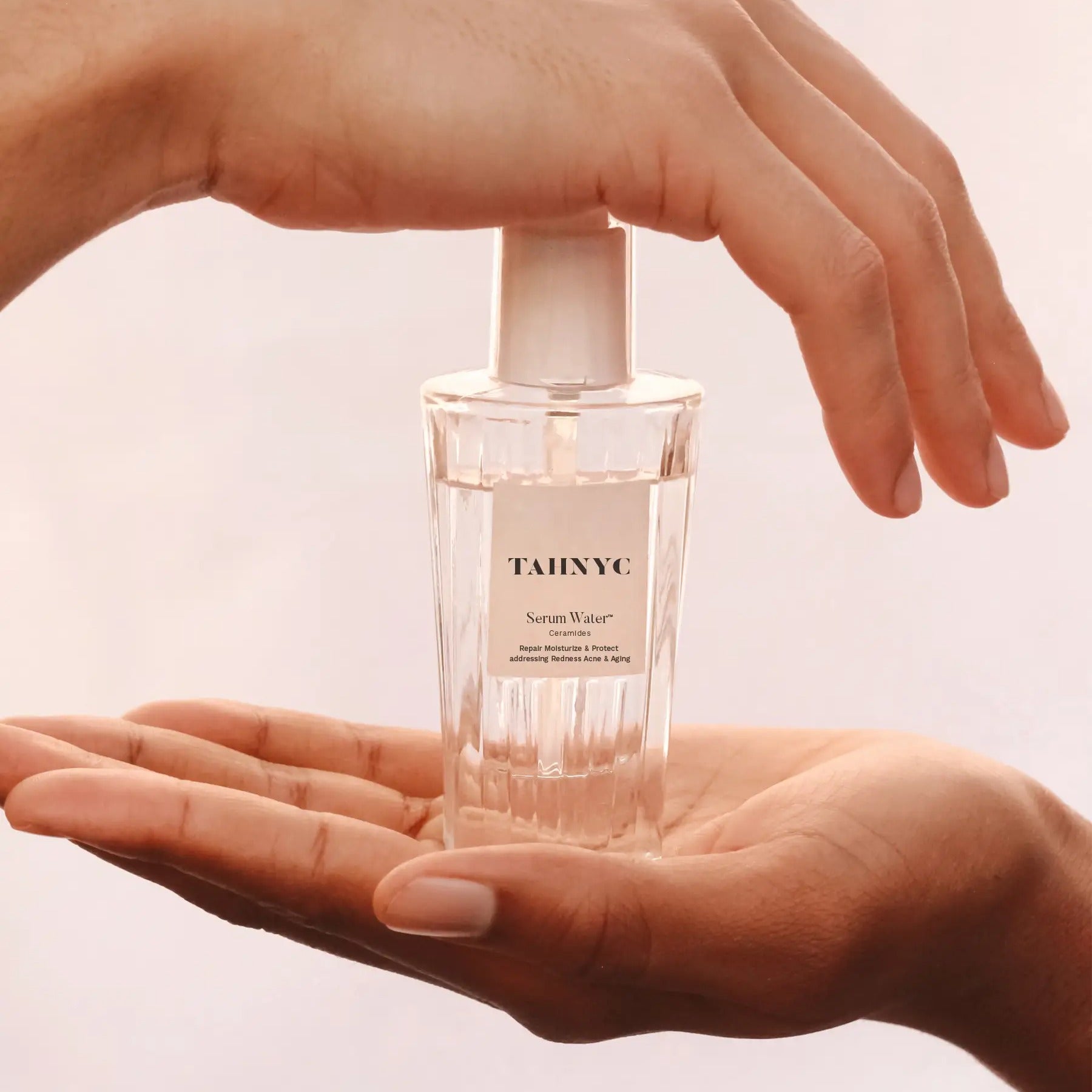 Hand holding a bottle of TAHNYC serum water against a light background