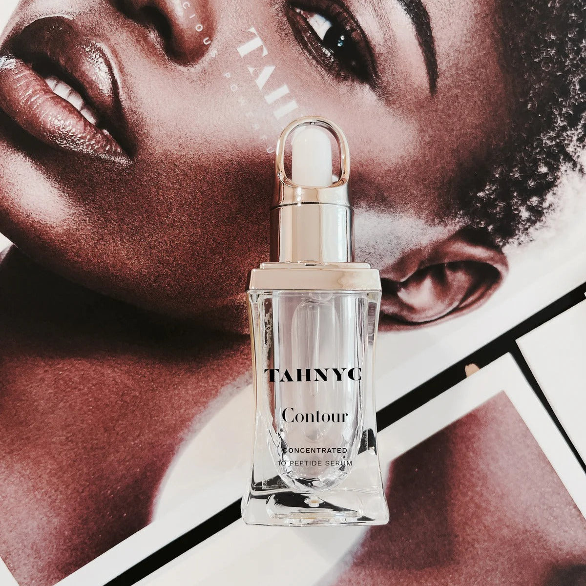 TAHNYC Contour Peptide Serum in a clear dropper bottle placed over a magazine page featuring a model’s face.