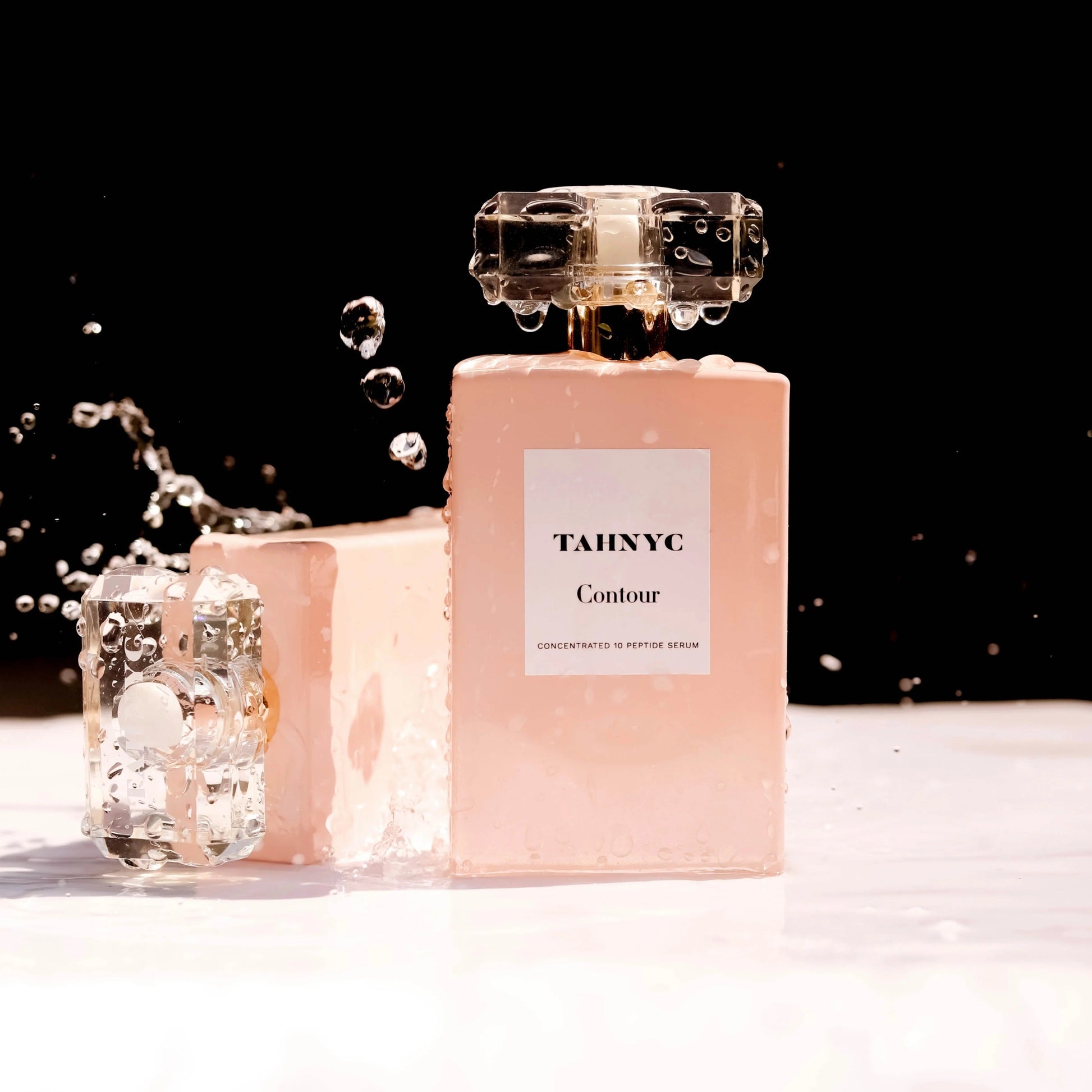 TAHNYC Contour Peptide Serum splashed with water droplets against a black background, highlighting hydration benefits.