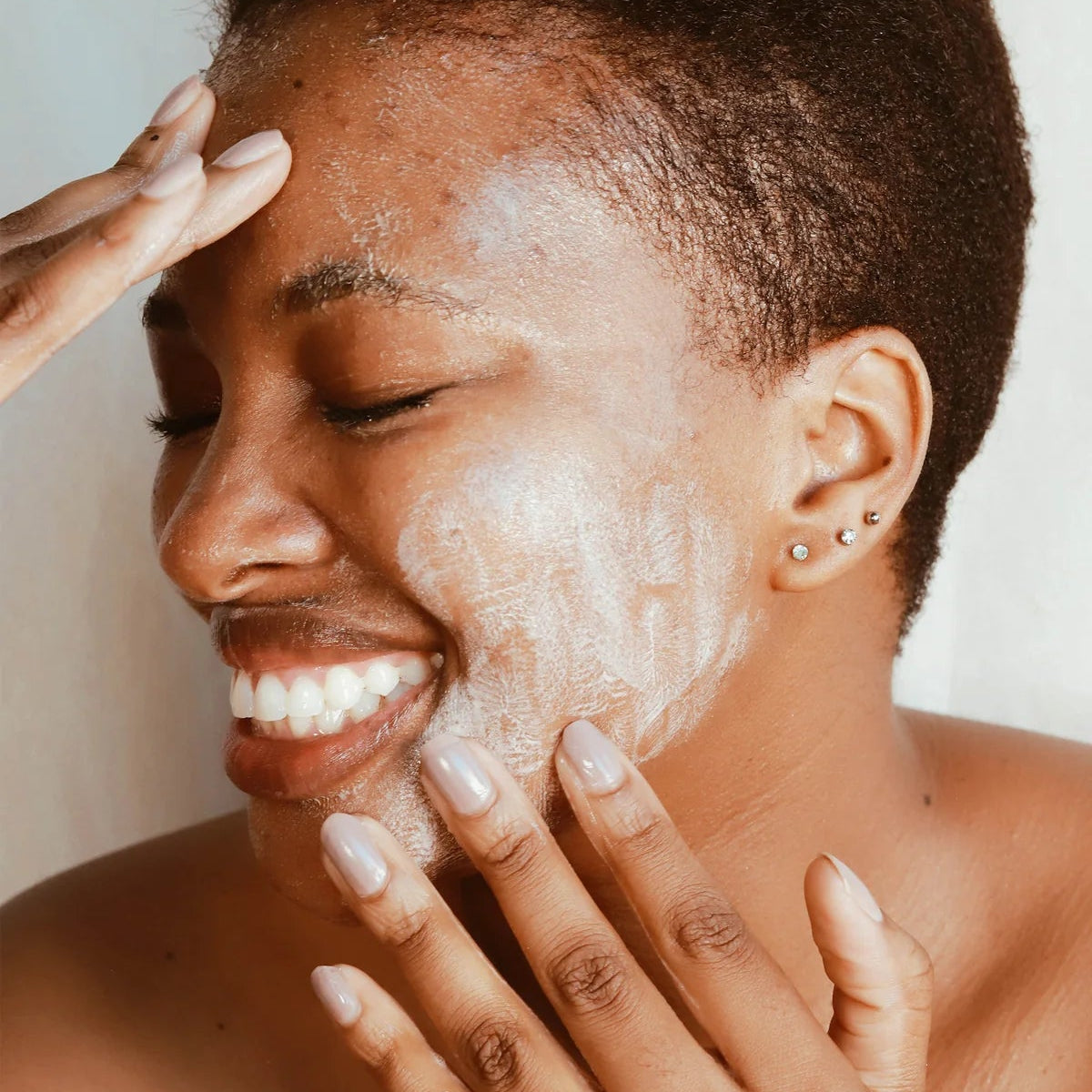 Person applying a white cream to their face with a neutral background