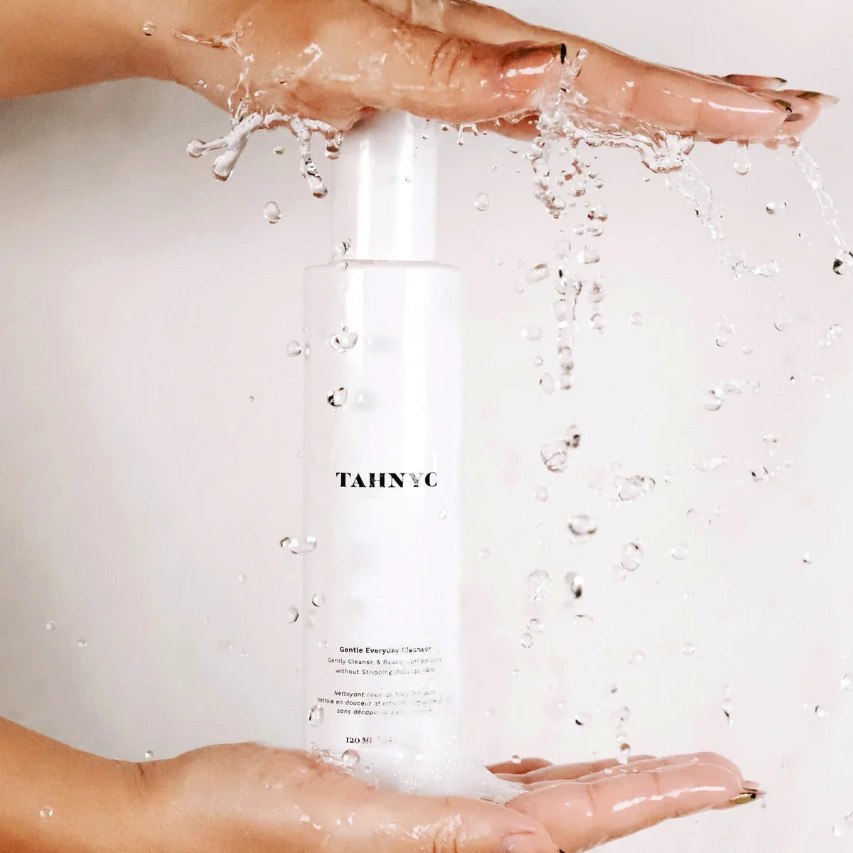Person holding a bottle of TAHINIC skincare product with water splashes.