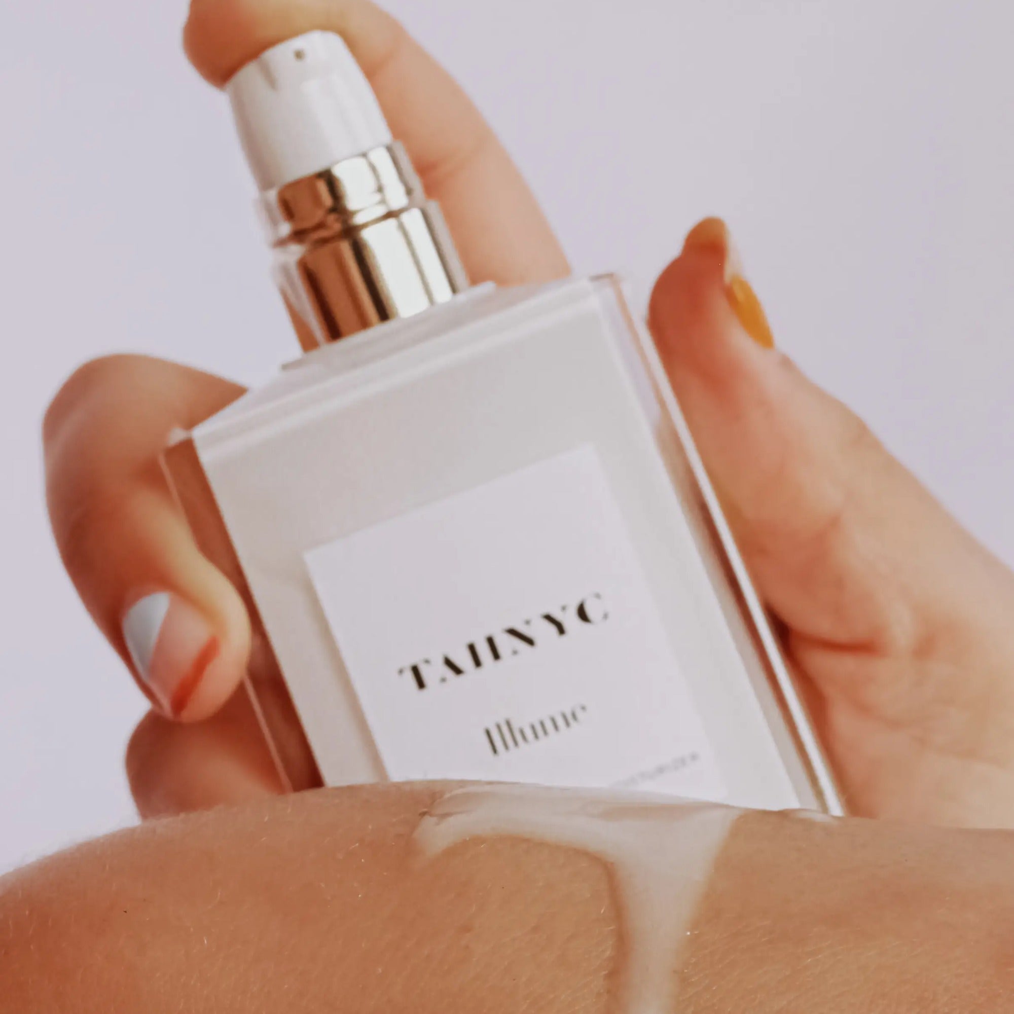 Hand holding a TAHNYC perfume bottle with a white label against a light background