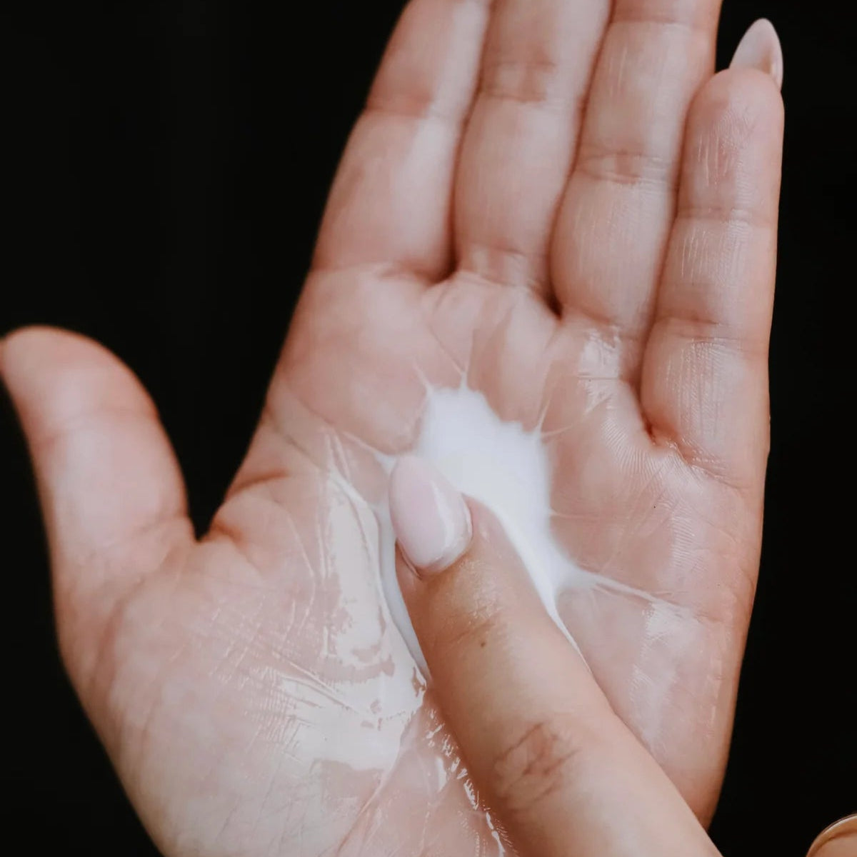 Hand holding a small amount of white cream against a black background
