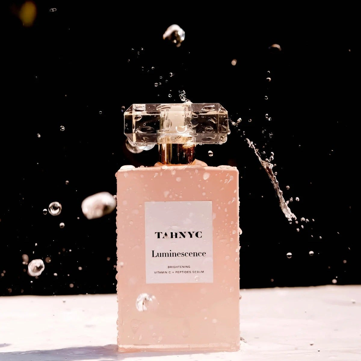 TAHNYC Luminescence Vitamin C + Peptides Serum bottle with water droplets captured mid-splash against black background – The Pharmacy Lab