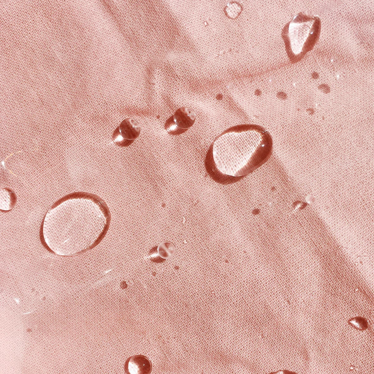 Water droplets resting on blush-pink textured fabric symbolizing hydration and softness – The Pharmacy Lab