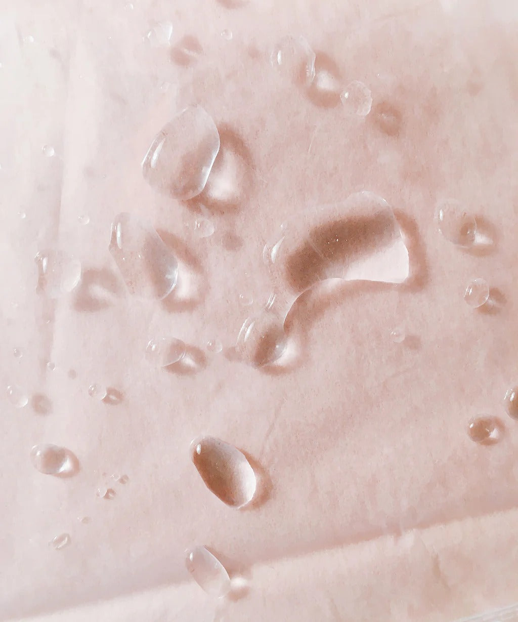 Water droplets on blush surface representing lightweight hydrating serum texture – The Pharmacy Lab