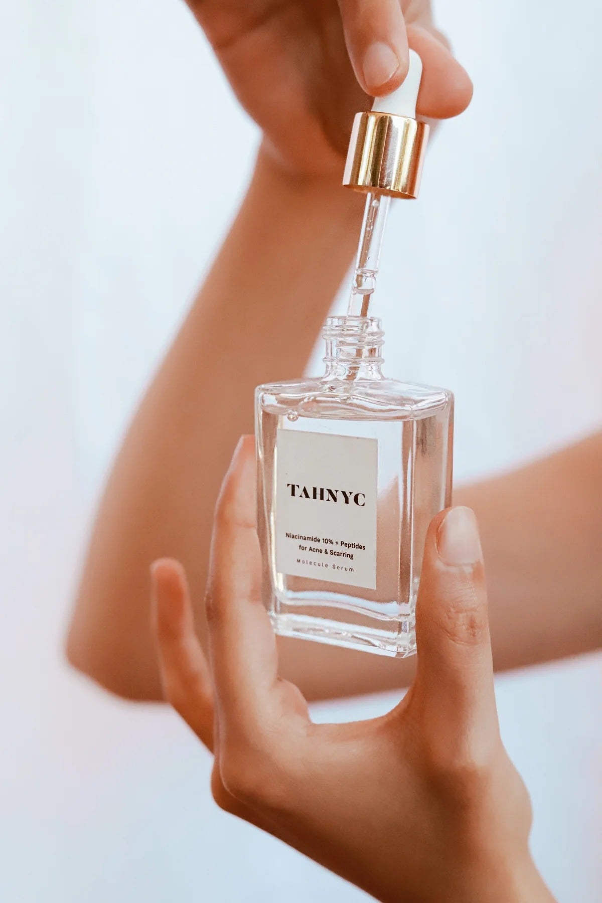Hands applying TAHNYC Niacinamide 10% + Peptides for Acne & Scarring serum from glass bottle – The Pharmacy Lab