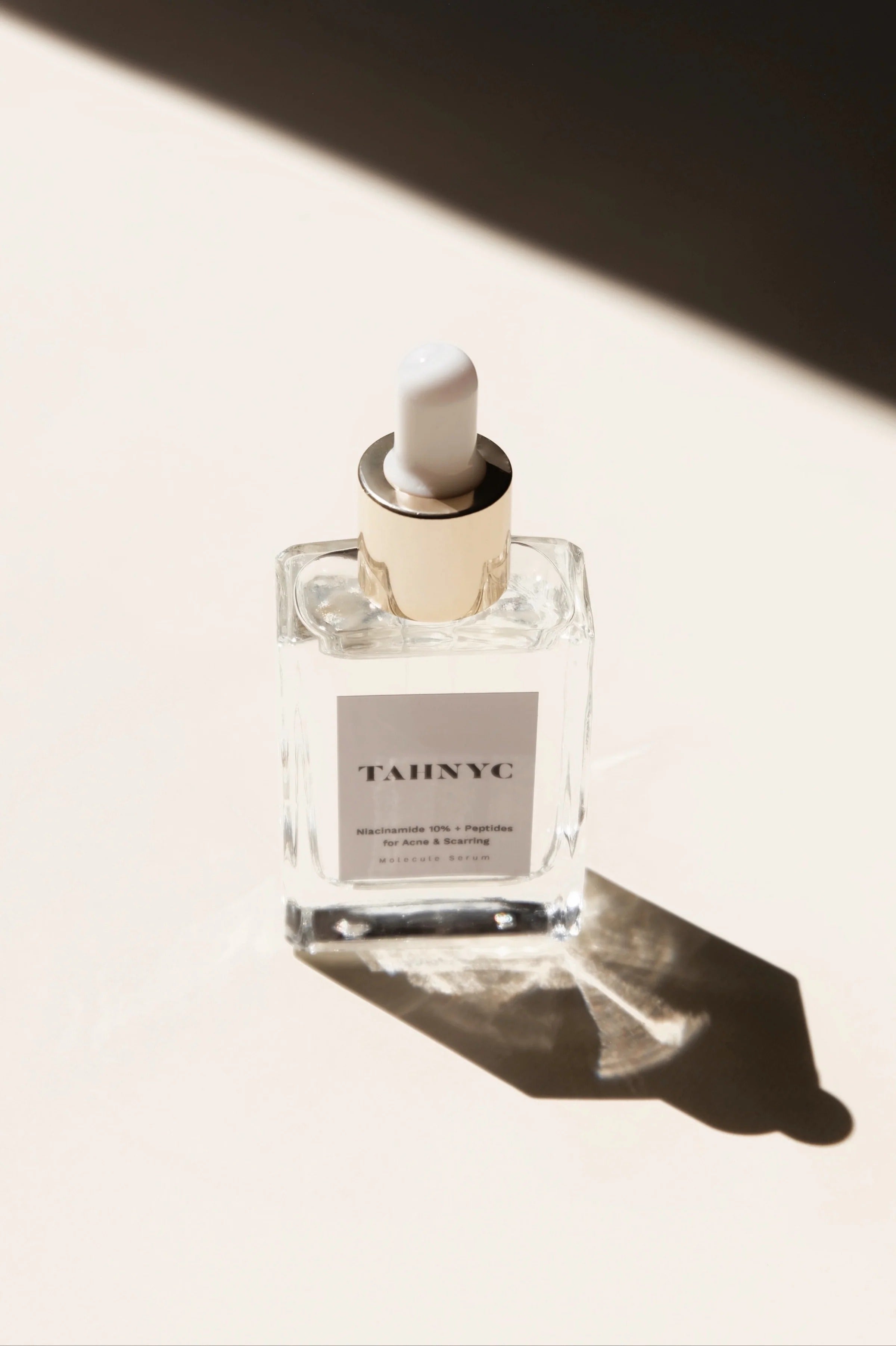 TAHNYC niacinamide serum bottle in warm light with long shadow – The Pharmacy Lab