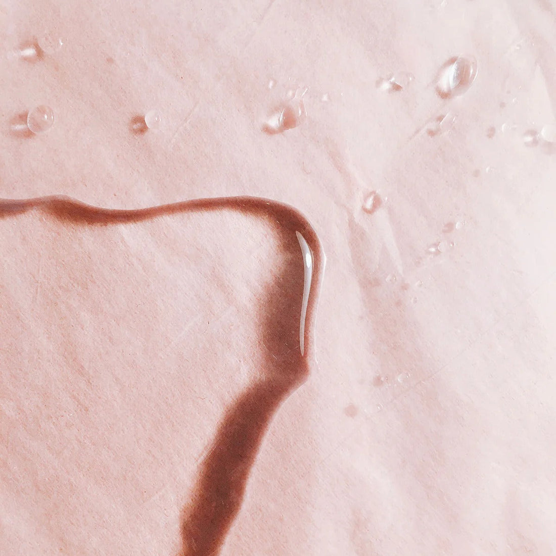 Water droplets on blush backdrop showing lightweight serum texture – The Pharmacy Lab