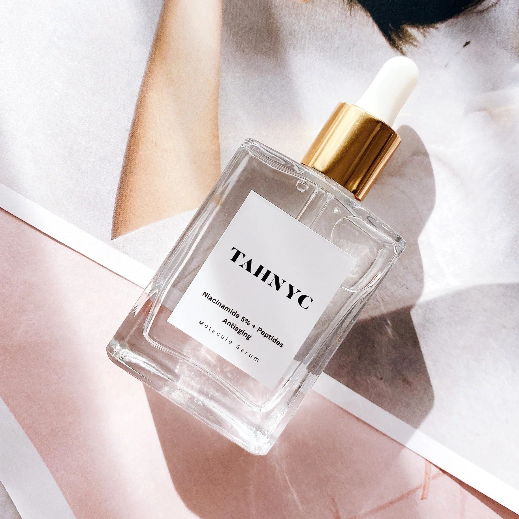 TAHNYC anti-aging serum bottle on pink and red floral background – The Pharmacy Lab