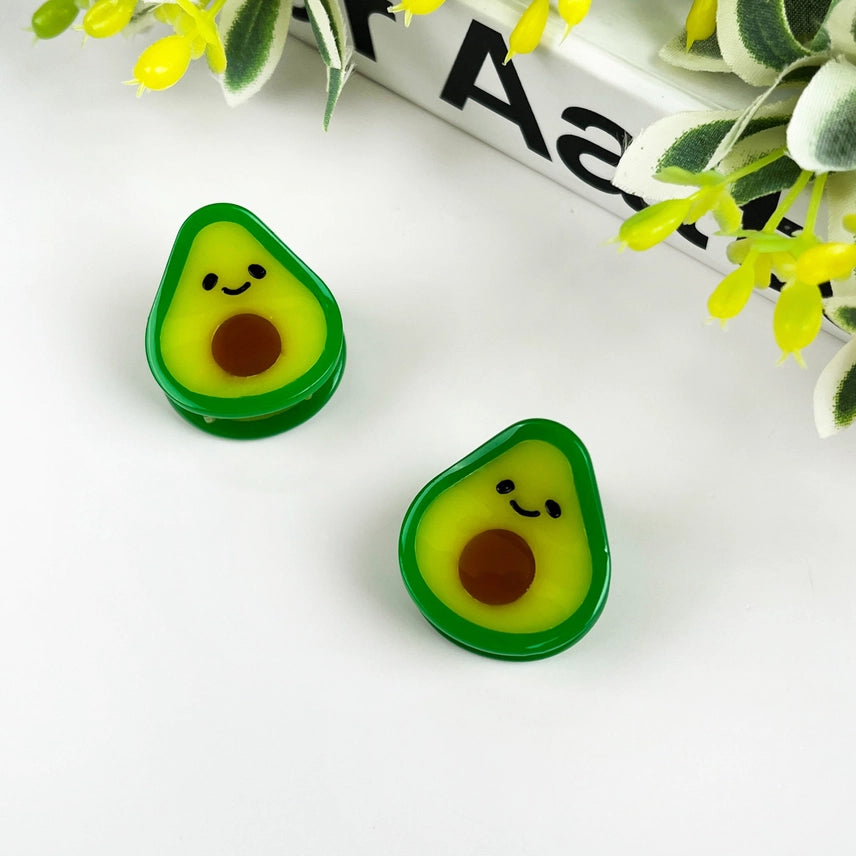Two avocado-shaped erasers with smiling faces on a white background with green leaves.