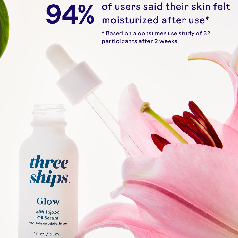 Three Ships Glow serum bottle with a dropper next to a pink flower on a white background