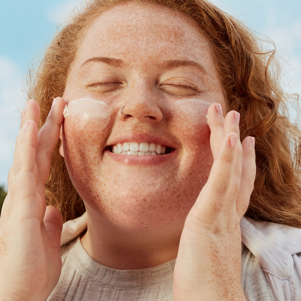 Woman applying sunscreen to her face with a clear sky background