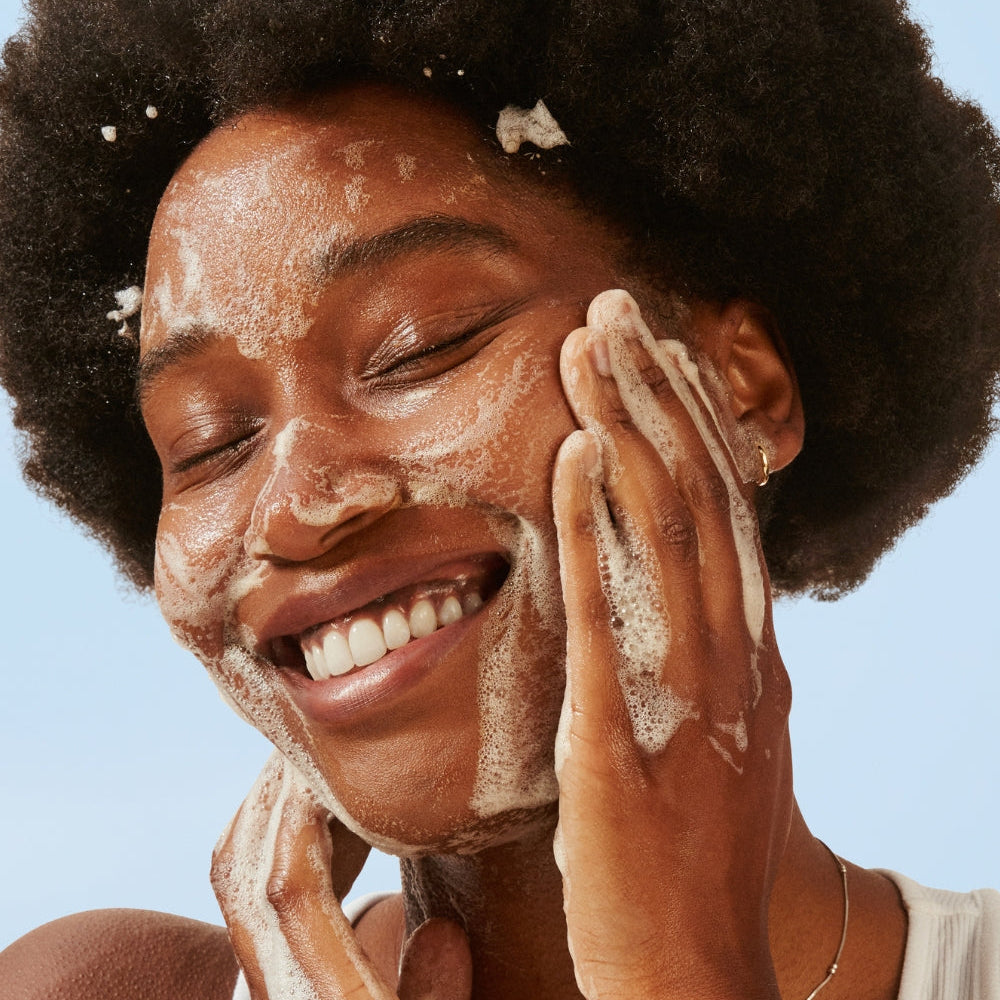 Person applying a facial scrub to their face against a clear blue sky
