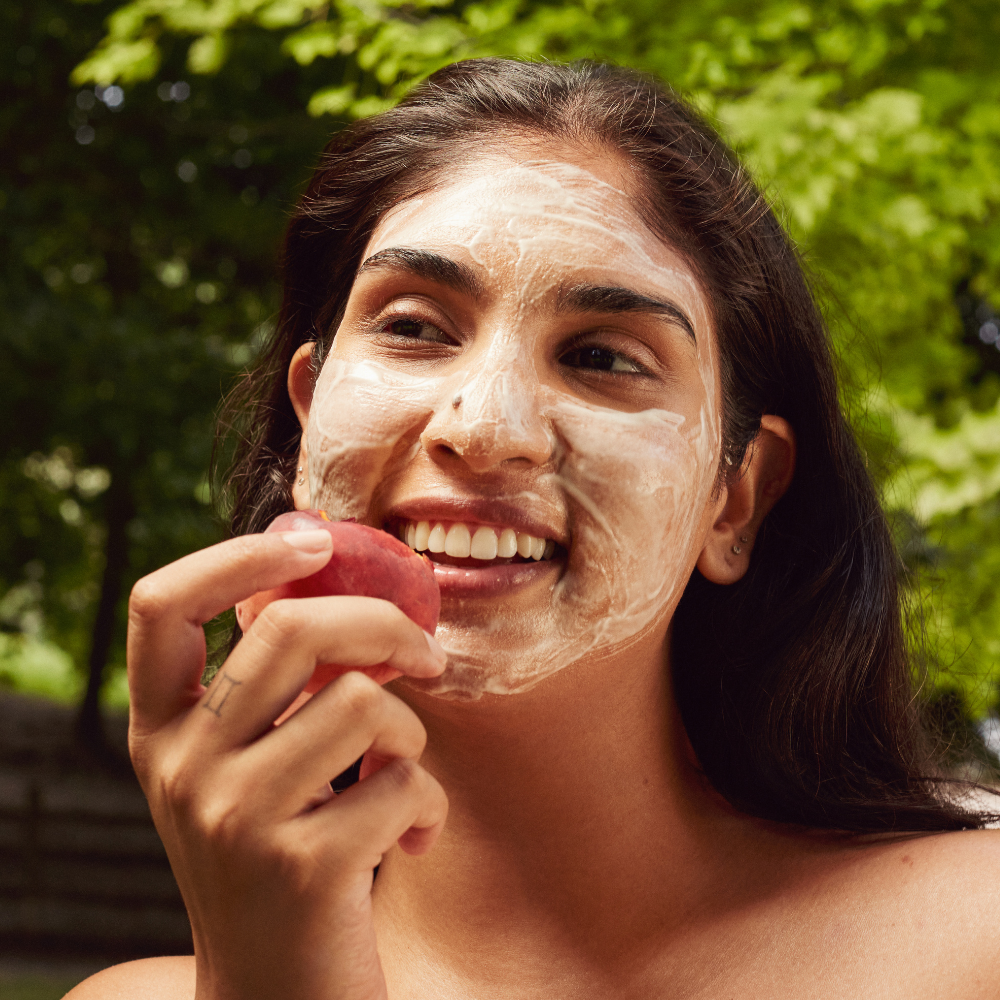 Woman applying a facial mask outdoors with greenery in the background