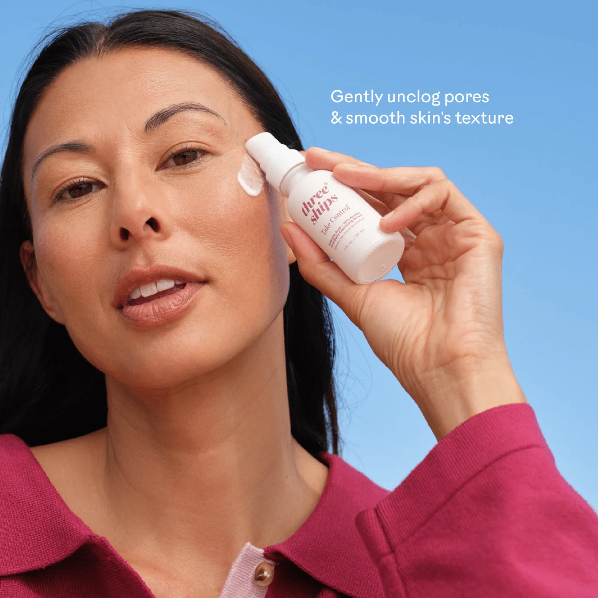 A woman holding a white bottle of Boss Body Oil while applying a white cream to her cheek against a solid blue background, with text reading 'Gently unclog pores & smooth skin's texture'.