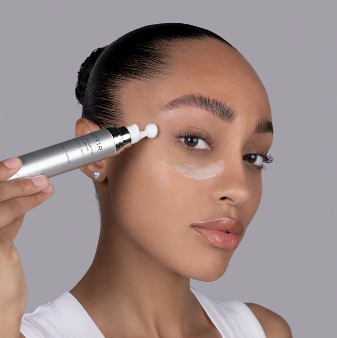 Woman applying skincare product to her face with a gray background