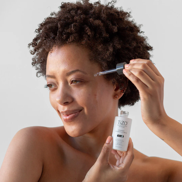 Woman applying TIZO skincare product to her face with a dropper.