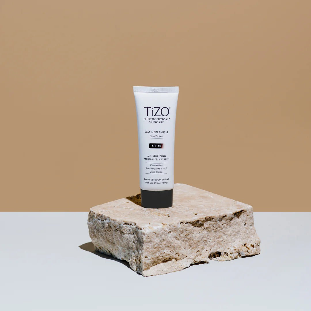 TiZO AM Replenish Non-Tinted SPF 40 Mineral Sunscreen displayed on a textured stone block against a neutral background for a clean skincare lifestyle aesthetic.