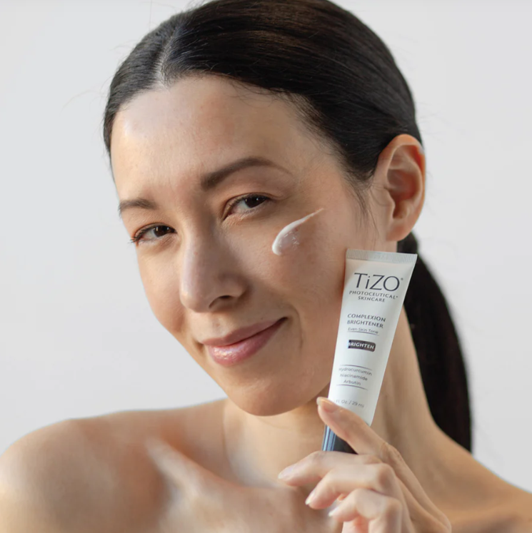 Woman applying TIZO skincare cream to her face with a white background