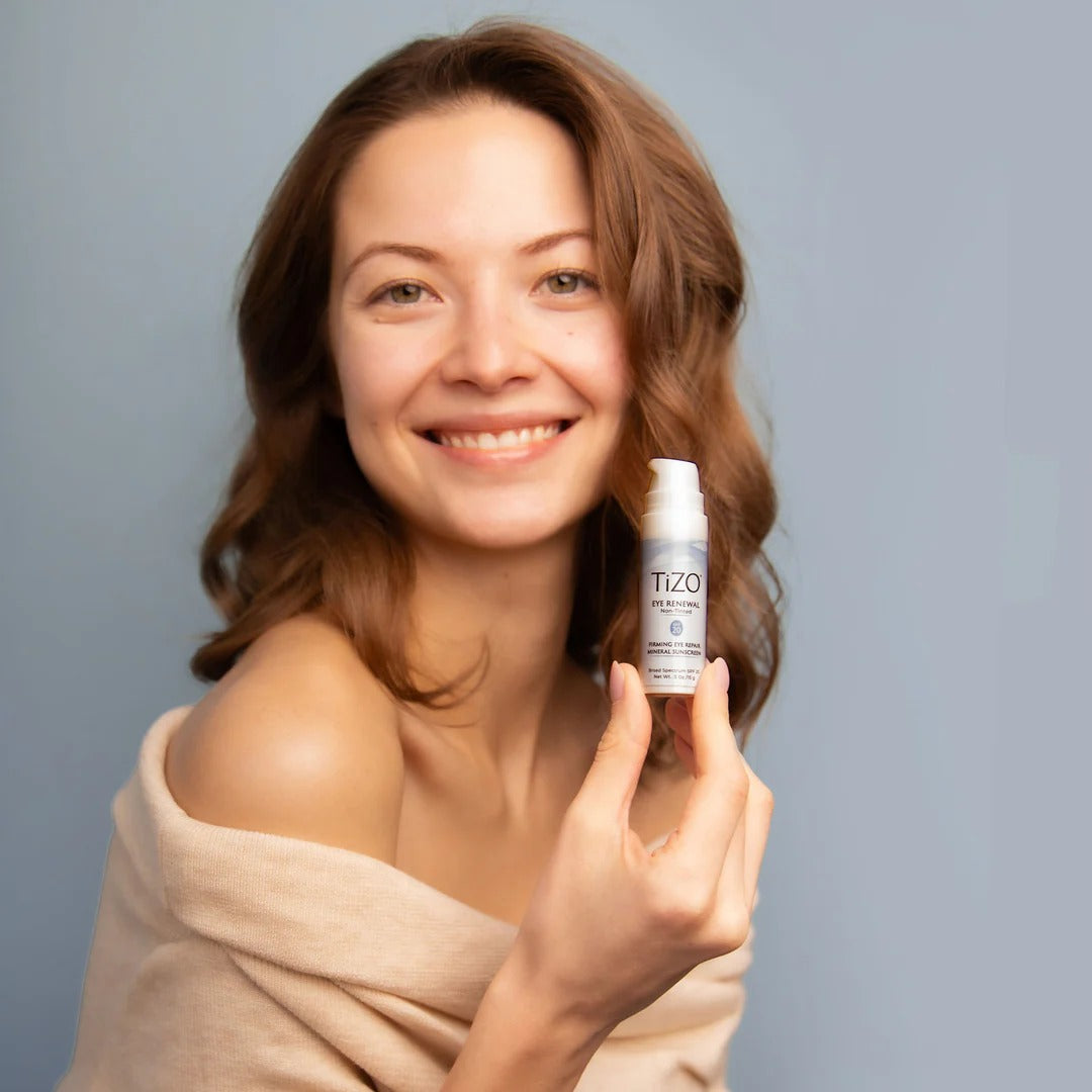 Woman holding a TIZO skincare bottle against a gray background