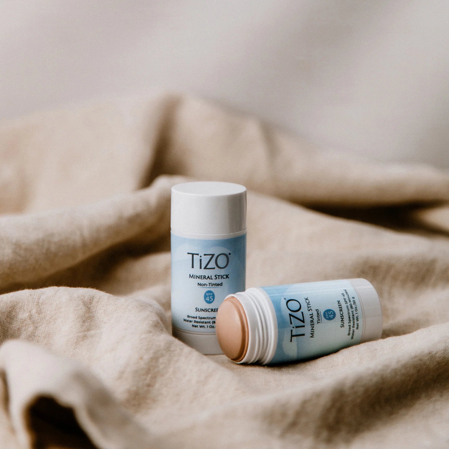 Two Tizo skincare sticks on a beige fabric background