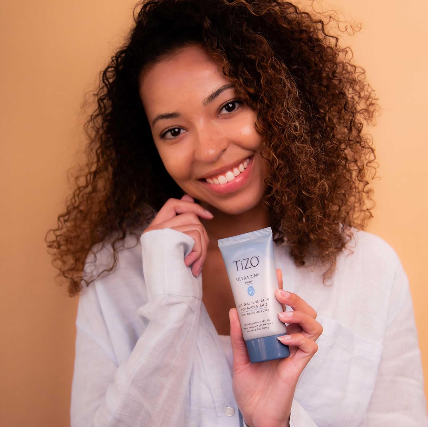 Woman holding a TIZO skincare product against a beige background