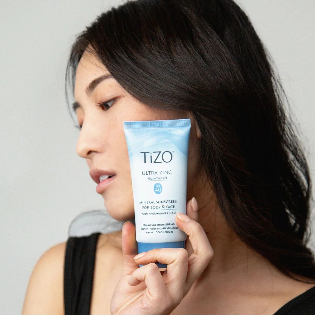 Woman holding a Tizo Ultra Zinc sunscreen tube against a neutral background