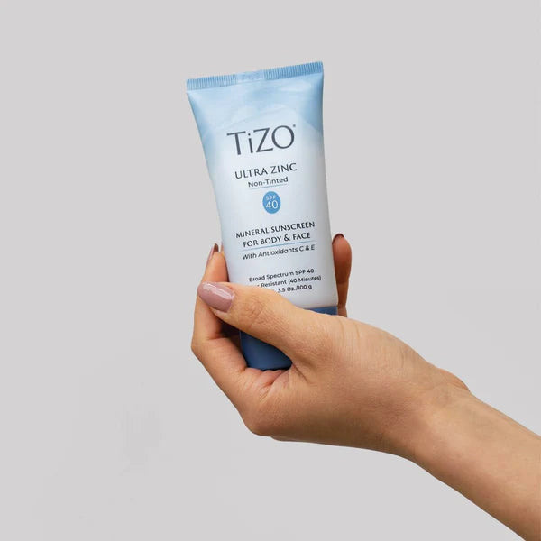 Hand holding a Tizo Ultra Zinc sunscreen tube against a gray background