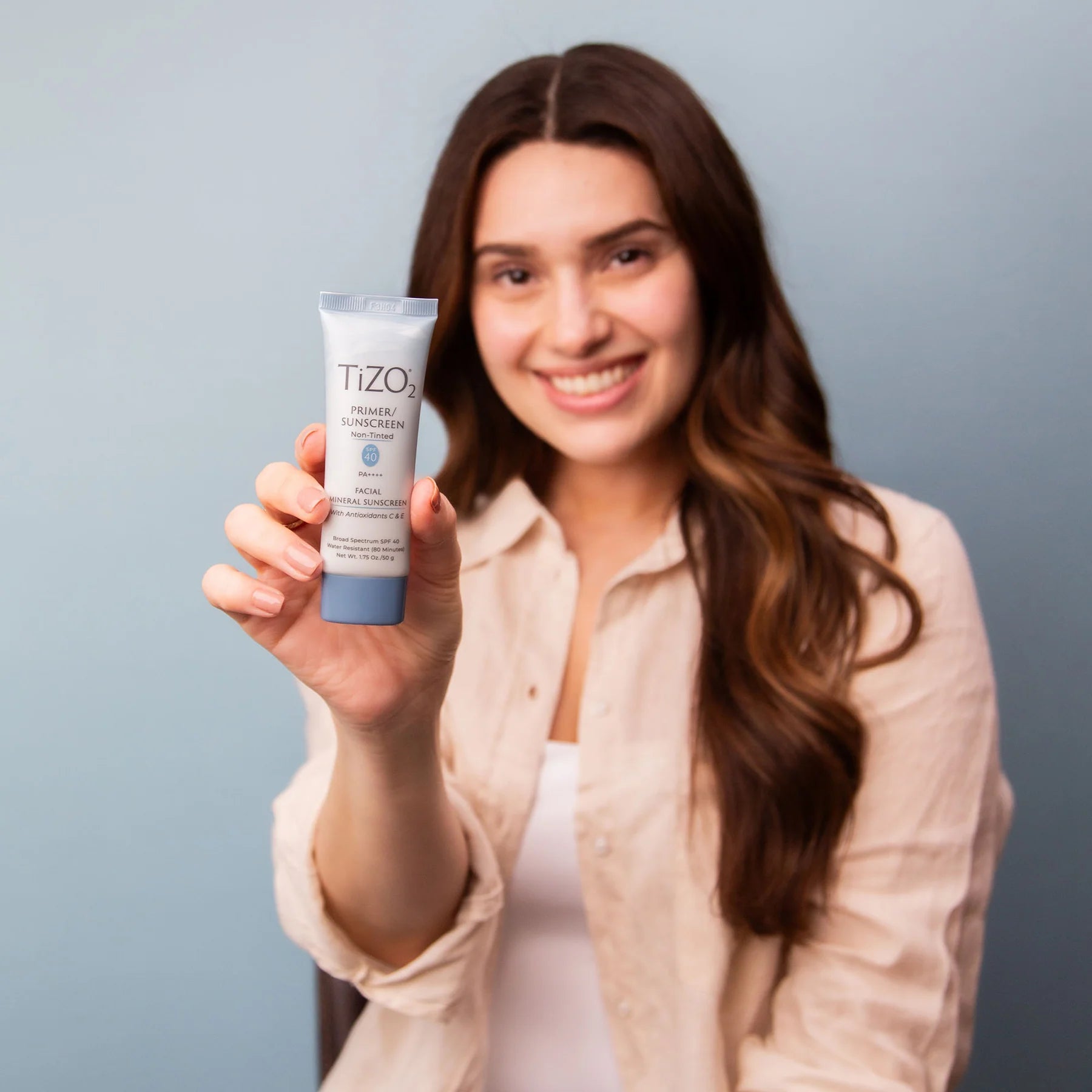 Woman holding a TIZONI skincare product against a gray background