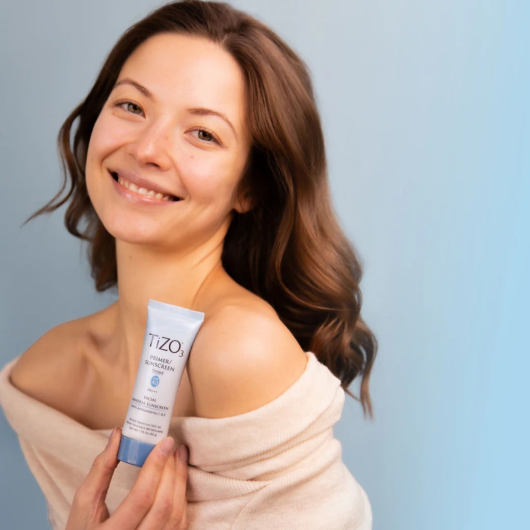 Woman holding a tube of Tizo skincare product against a light blue background